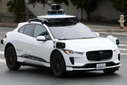 White Waymo vehicle with roof-mounted and exterior driving sensors.